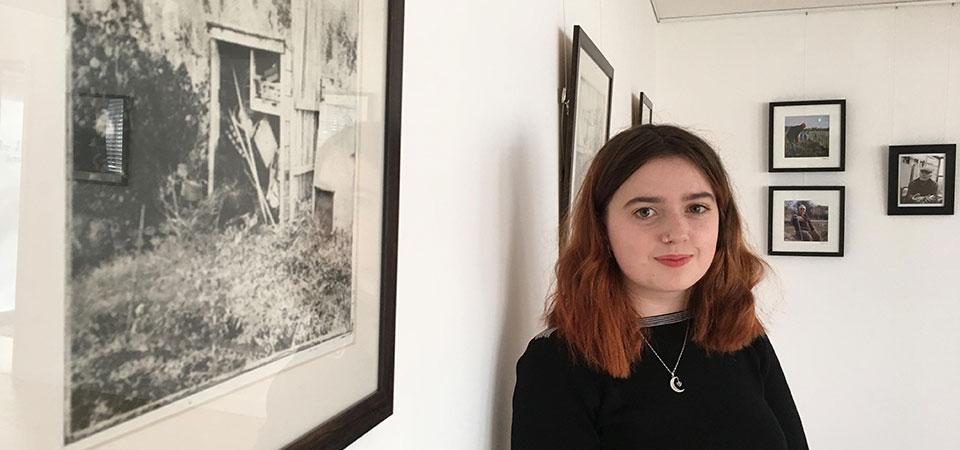 young white woman with dark hair standing in front of black and white photo of an allotment site