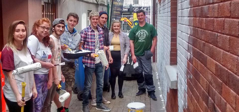 a group of young people with paint overalls and brushes standing in a brick alleyway